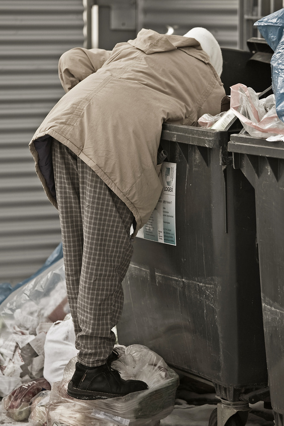 eine Frau steht auf einem Schneehaufen und wühlt in einem Müllcontainer