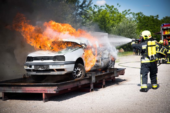 Brennender PKW wird von Feuerwehrmann gelöscht
