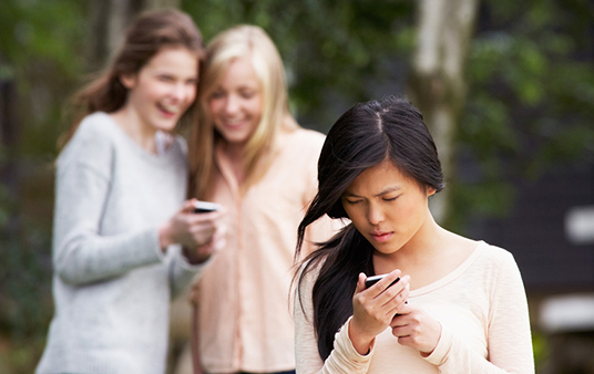 Mädchen lachen über einen Smartphone-Eintrag. Anderes Mädchen steht im Vordergrund